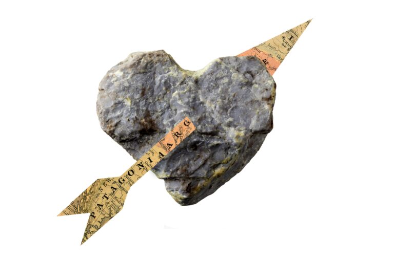 Heart shaped rock with a spear shaped, paper piercing through it. The paper is made from a map.